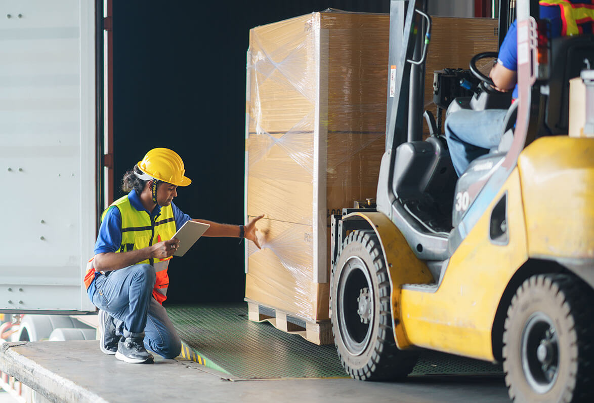 Woman in safety gear with a tablet inspects a pallet on a forklift